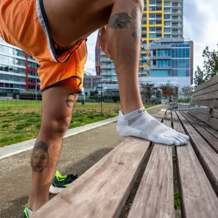 Man in orange shorts and white toe socks stretching on a wooden bench