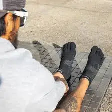Man wearing black toe socks and white cap, sitting on a paved surface