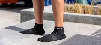 Person wearing black ankle socks with grey stripes on a concrete surface