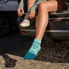 Woman tying shoelaces on a white running shoe, wearing a blue toe sock