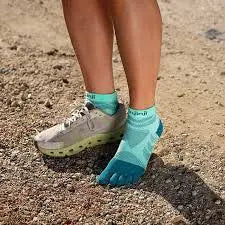 Person wearing turquoise toe socks and one running shoe on a dirt path