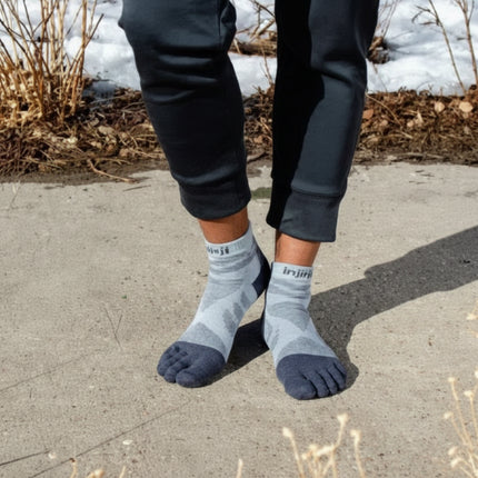 Person wearing grey toe socks and black pants standing on a paved surface