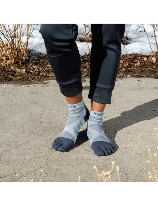 Person wearing grey toe socks and black pants standing on a paved surface