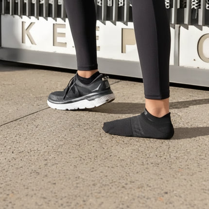 Person wearing black leggings, one foot in a black sneaker, the other in a black sock
