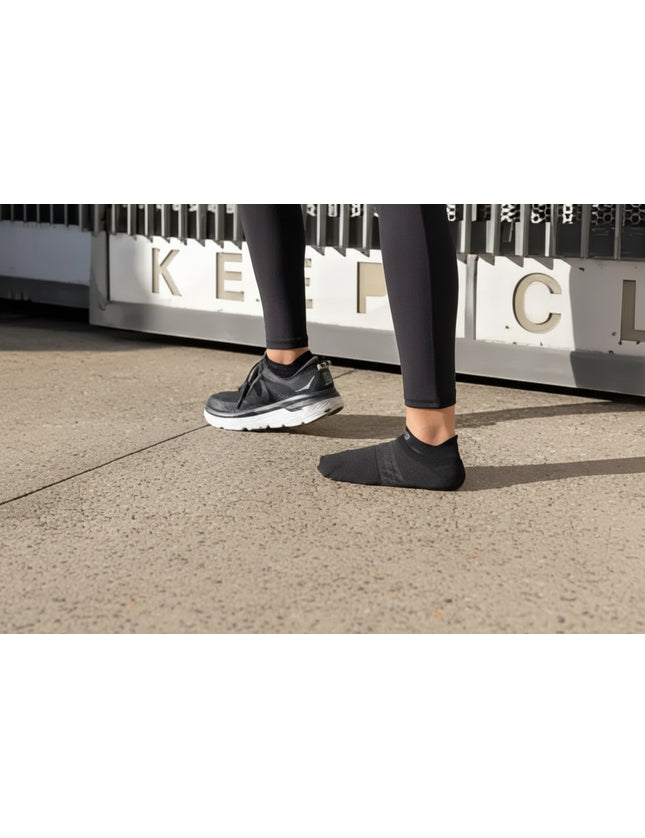 Person wearing black leggings, one foot in a black sneaker, the other in a black sock