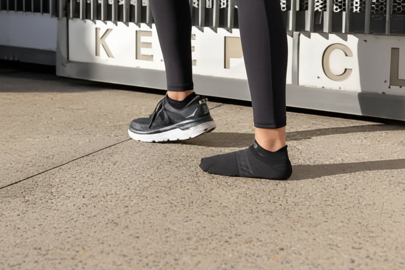 Person wearing black leggings, one foot in a black sneaker, the other in a black sock