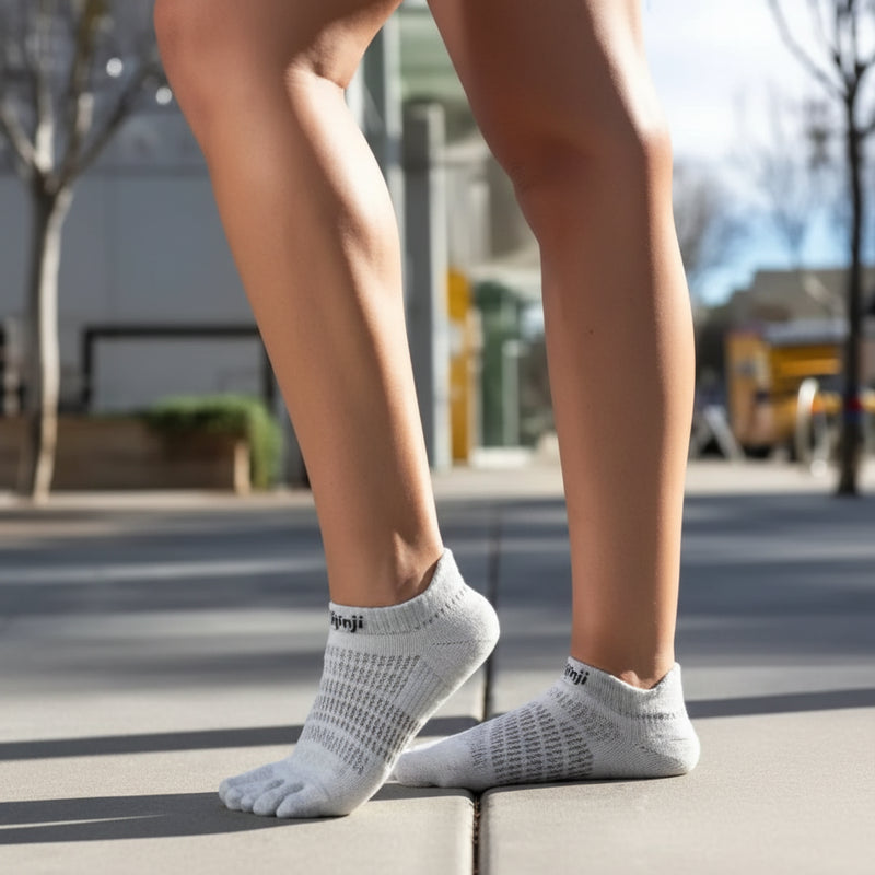 Person wearing light grey toe socks and standing on a sidewalk