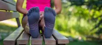 Person wearing grey toe socks with pink accents, resting feet on a wooden bench outdoors