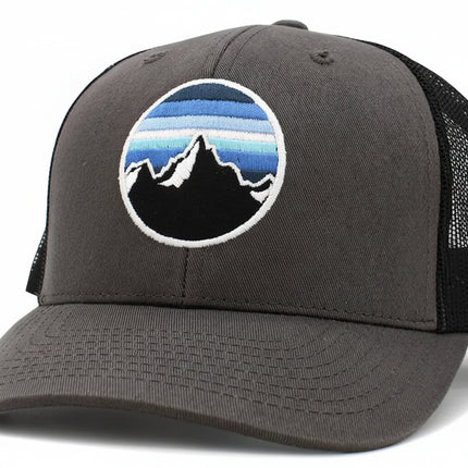 Grey trucker hat with a circular patch featuring black mountains and blue sky stripes