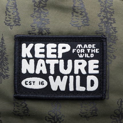Close-up of a rectangular embroidered patch on olive green camouflage fabric. The patch is black with white text reading 'KEEP NATURE WILD' and smaller text 'MADE FOR THE WILD' and 'EST 16'.