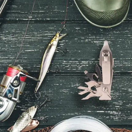 Fishing gear including a reel, lures, and a multi-tool on a dark wooden surface