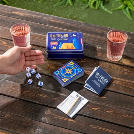 Hand next to dice, cards, and game instructions on a wooden table with two glasses