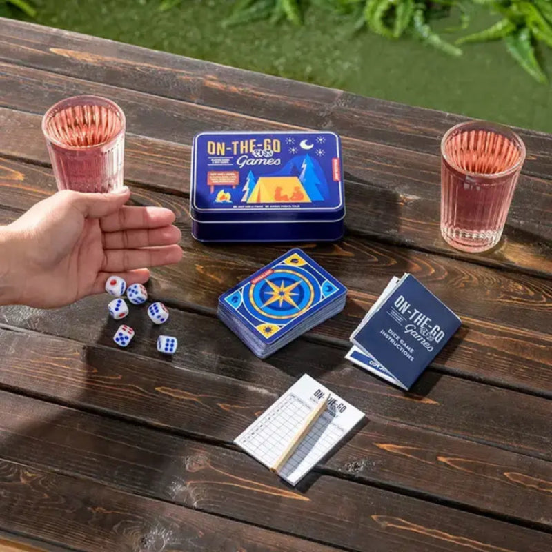 Hand next to dice, cards, and game instructions on a wooden table with two glasses