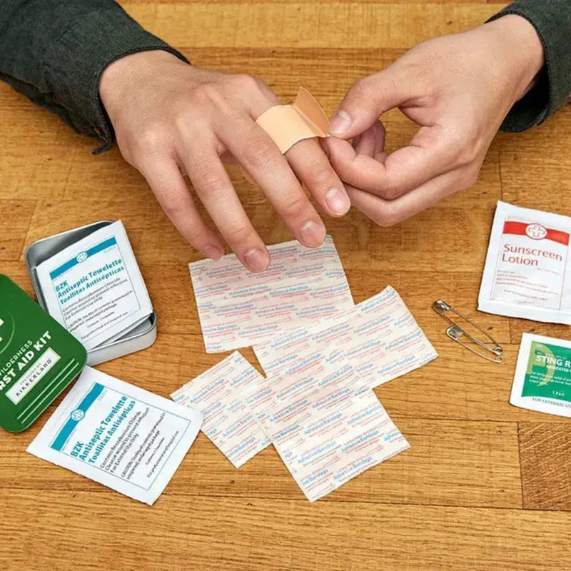 Person applying a bandage to their finger, surrounded by first aid kit contents