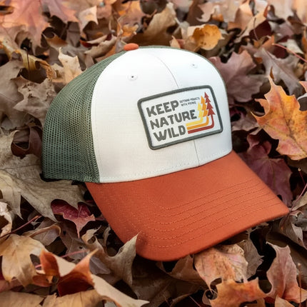 White, green, and orange cap with Keep Nature Wild patch on autumn leaves