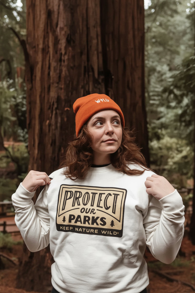 Woman in orange beanie and white Protect Our Parks sweatshirt in a forest