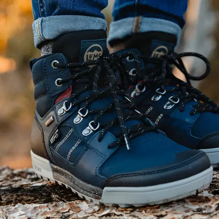 Pair of blue Lems waterproof boots with black laces and grey soles on a tree trunk