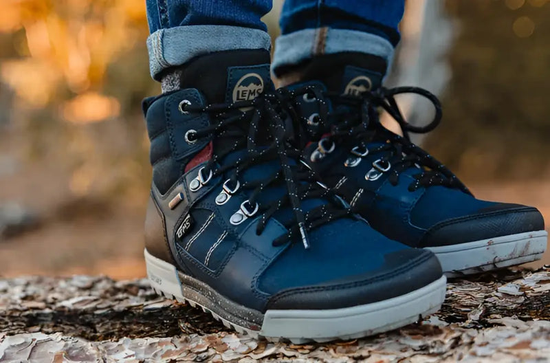 Pair of blue Lems waterproof boots with black laces and grey soles on a tree trunk