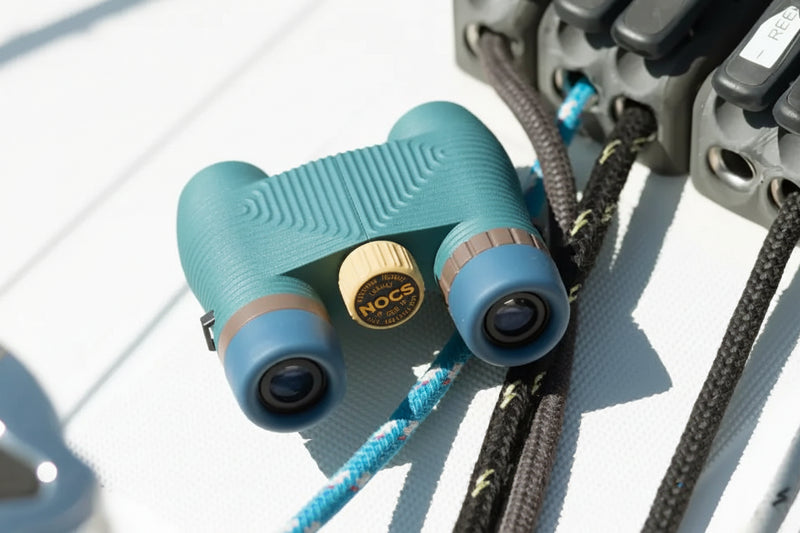 Teal Nocs Provisions binoculars with blue and brown accents on a boat deck with ropes