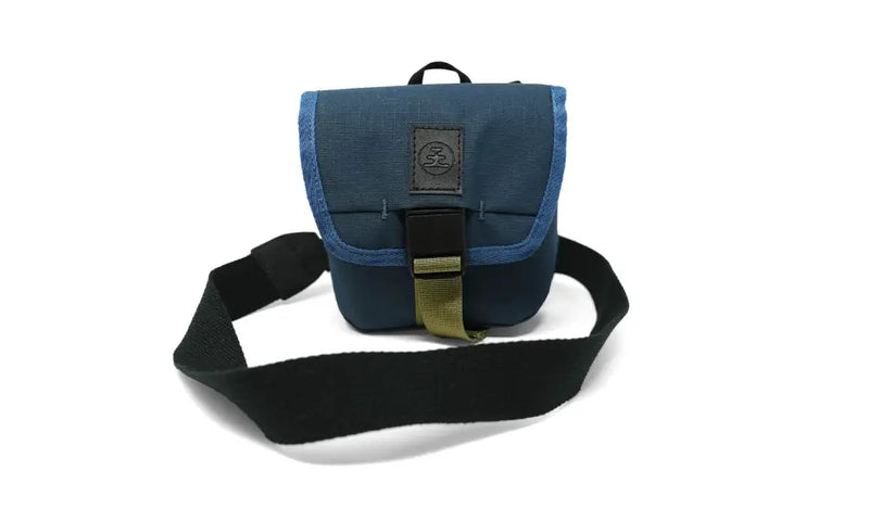 Blue camera bag with a black strap and olive green buckle on a white background