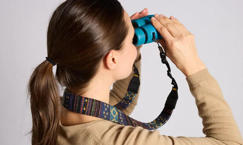 Woman with brown hair in a ponytail looking through blue binoculars with a patterned strap