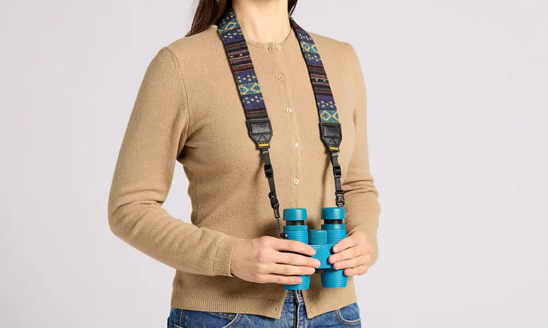 Woman wearing a patterned strap holding a pair of blue binoculars