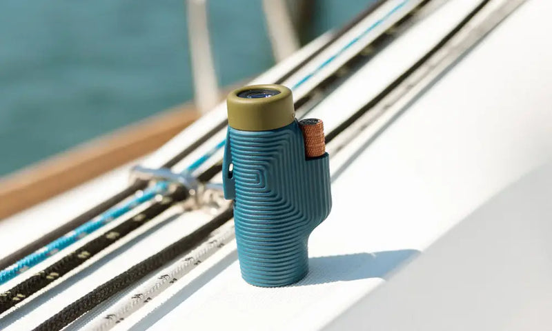 Blue monocular with an olive green top and orange focus wheel, sitting on a white boat deck