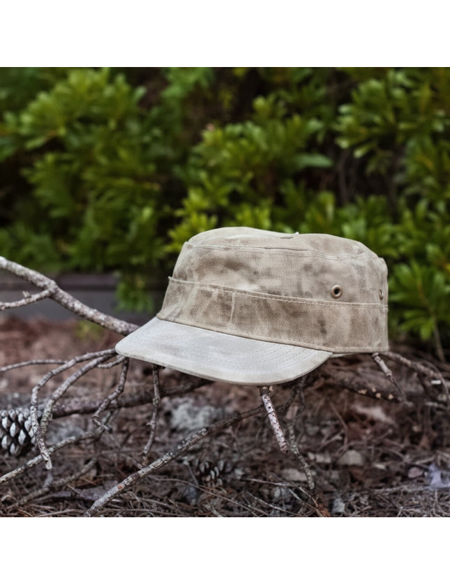 Tan canvas military-style cap with a brim, resting on a bed of pine needles and small branches