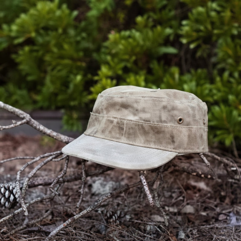 Tan canvas military-style cap with a brim, resting on a bed of pine needles and small branches