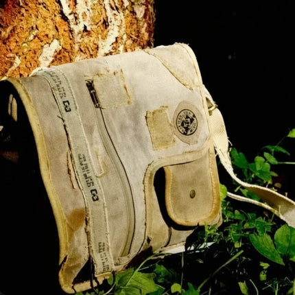 Vintage canvas shoulder bag with a flap closure and adjustable strap, resting against a tree trunk