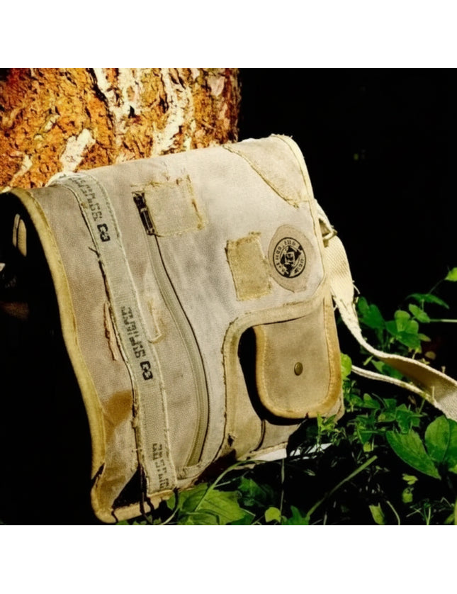 Vintage canvas shoulder bag with a flap closure and adjustable strap, resting against a tree trunk