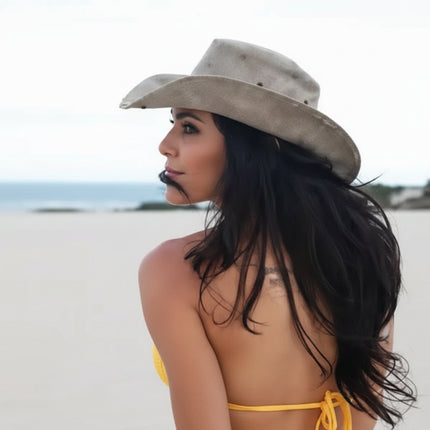 Woman in a cowboy hat and yellow bikini top looking over her shoulder at the ocean