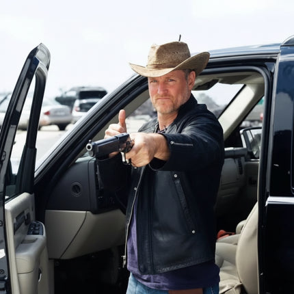 Man in cowboy hat and leather jacket holding a handgun, standing by an open car door