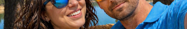 Couple wearing sunglasses, woman in blue sunglasses and man in red sunglasses, outdoors by a lake