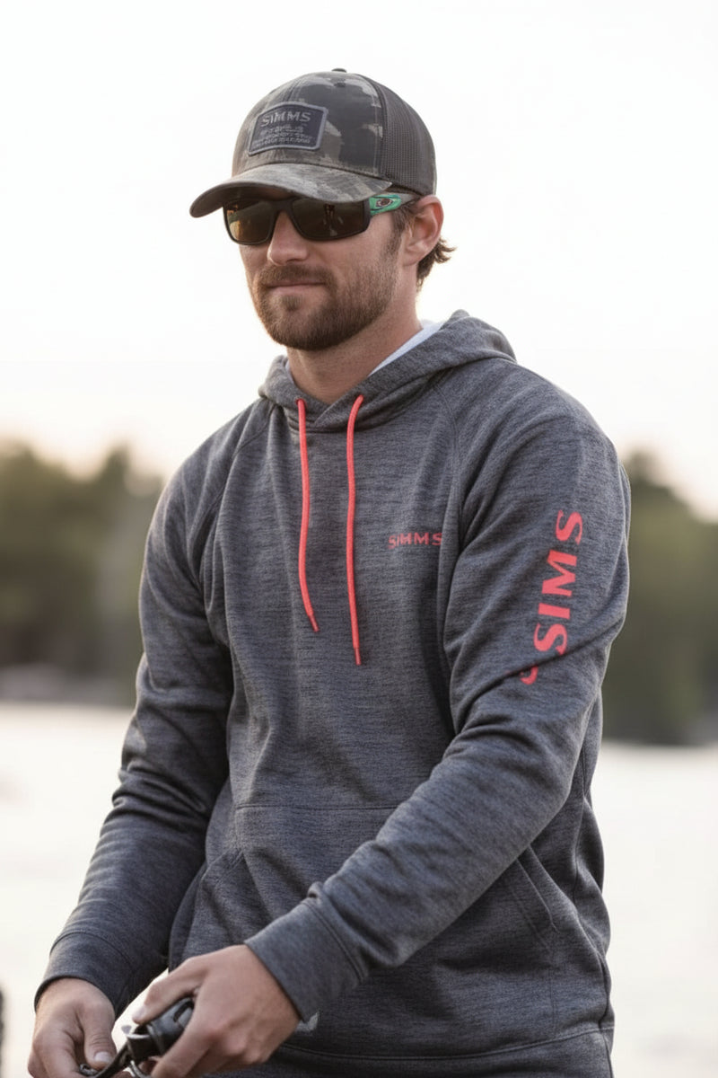 Man wearing a grey hoodie, sunglasses, and a cap, holding fishing gear