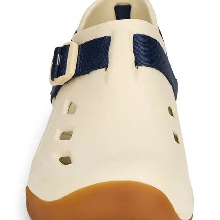 Cream-colored shoe with a brown sole and a navy blue strap with a cream buckle