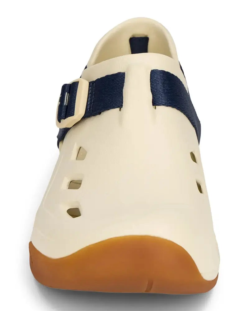 Cream-colored shoe with a brown sole and a navy blue strap with a cream buckle