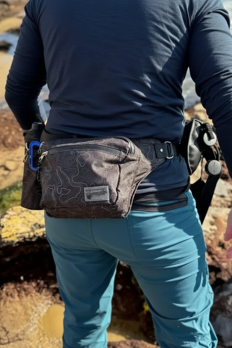 Person wearing a dark blue shirt and teal pants with a patterned fanny pack and water bottle