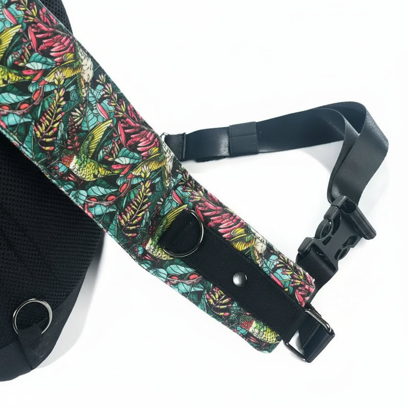 Close up of a bag strap with a colorful bird and leaf pattern, black webbing, and a plastic buckle