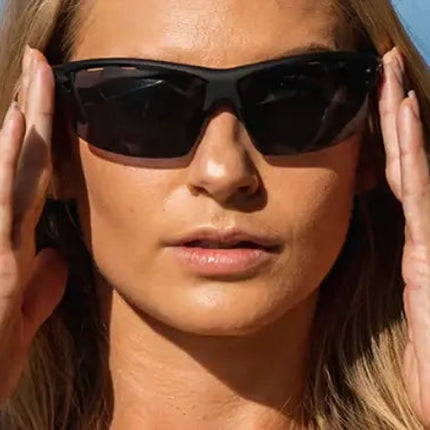 Woman wearing black sunglasses with hands near temples, blue sky background