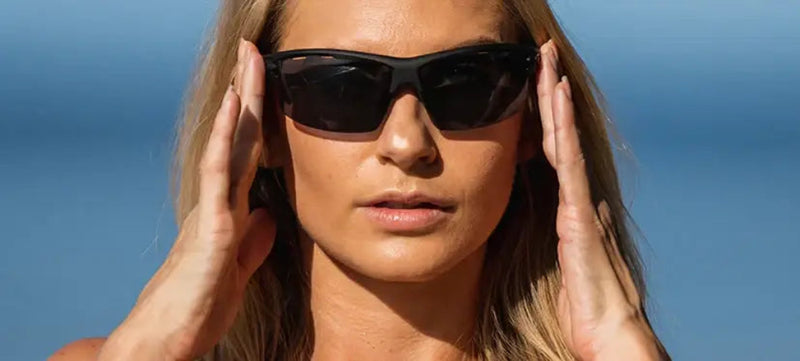 Woman wearing black sunglasses with hands near temples, blue sky background
