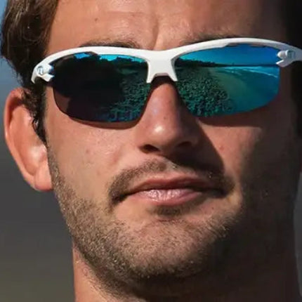 Man wearing white sunglasses with blue reflective lenses, showing a beach scene reflection