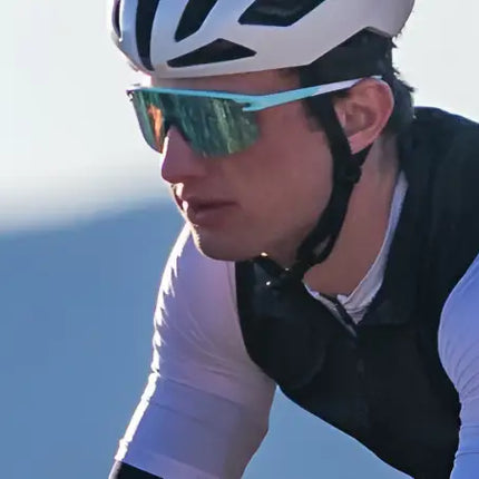 Cyclist wearing a white helmet, black vest, white long-sleeved shirt, and blue mirrored sunglasses