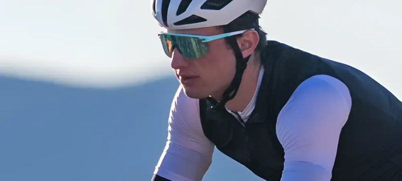 Cyclist wearing a white helmet, black vest, white long-sleeved shirt, and blue mirrored sunglasses