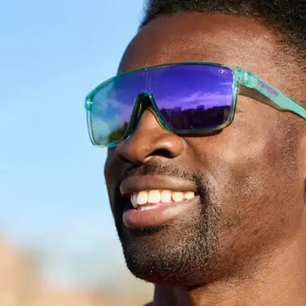 Man with dark skin and short dark hair wearing teal sunglasses with purple lenses