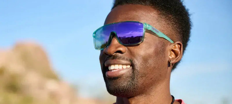 Man with dark skin and short dark hair wearing teal sunglasses with purple lenses