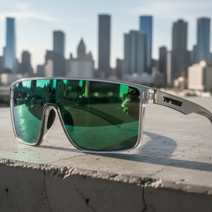 Silver frame sunglasses with green reflective lenses on a concrete ledge, city skyline in background