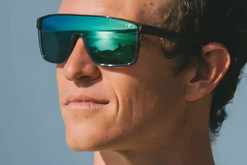 Man wearing sunglasses with a reflection of a lake and trees