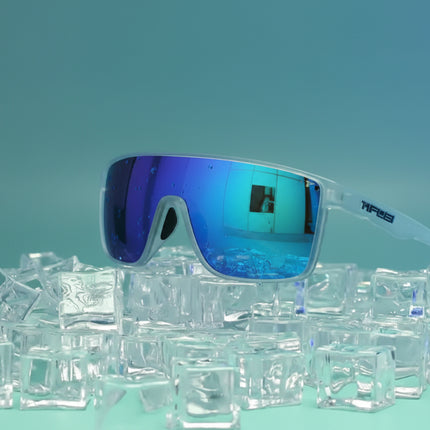 Tifosi sunglasses with blue mirrored lenses and clear frames, resting on a pile of ice cubes