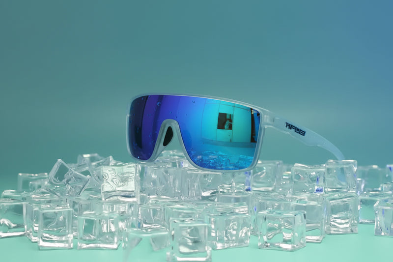Tifosi sunglasses with blue mirrored lenses and clear frames, resting on a pile of ice cubes